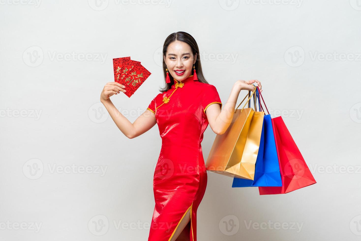 Portrait of smiling happy Asian woman carrying colorful bags and showing red envelopes for Chinese new year shopping concepts, text means great luck great profit photo