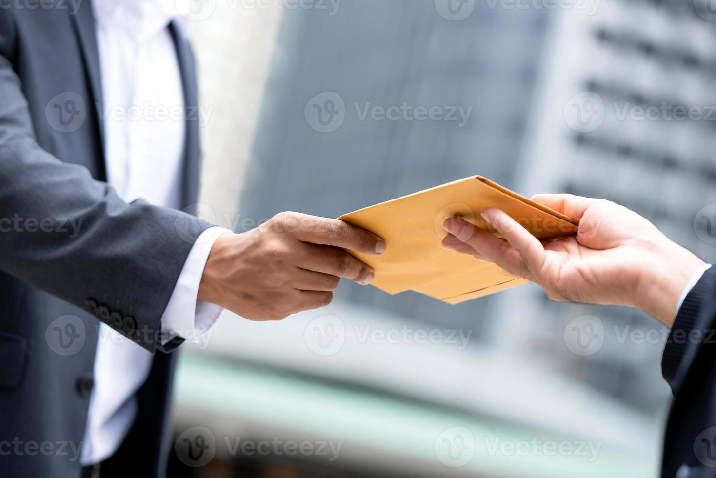 Close up portrait of  businessman hand recieving yellow envelope from boss in urban city background photo