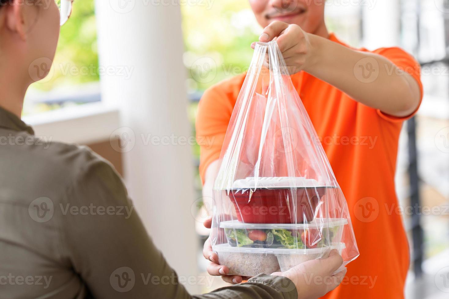 Delivery man giving lunch box meal in the bag to customer that ordered online at home photo