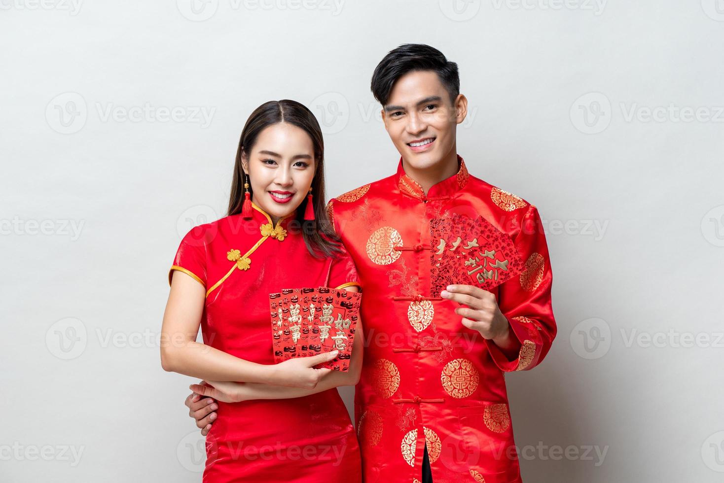 feliz pareja asiática con trajes orientales tradicionales sosteniendo sobres rojos o ang pao con fondo gris claro para conceptos de año nuevo chino, los textos significan gran suerte, gran beneficio foto