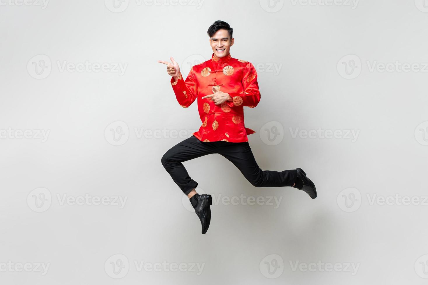 Portrait of smiling handsome Asian man in traditional chinese attire smiling and pointing hands to empty space aside in light gray isolated studio background photo