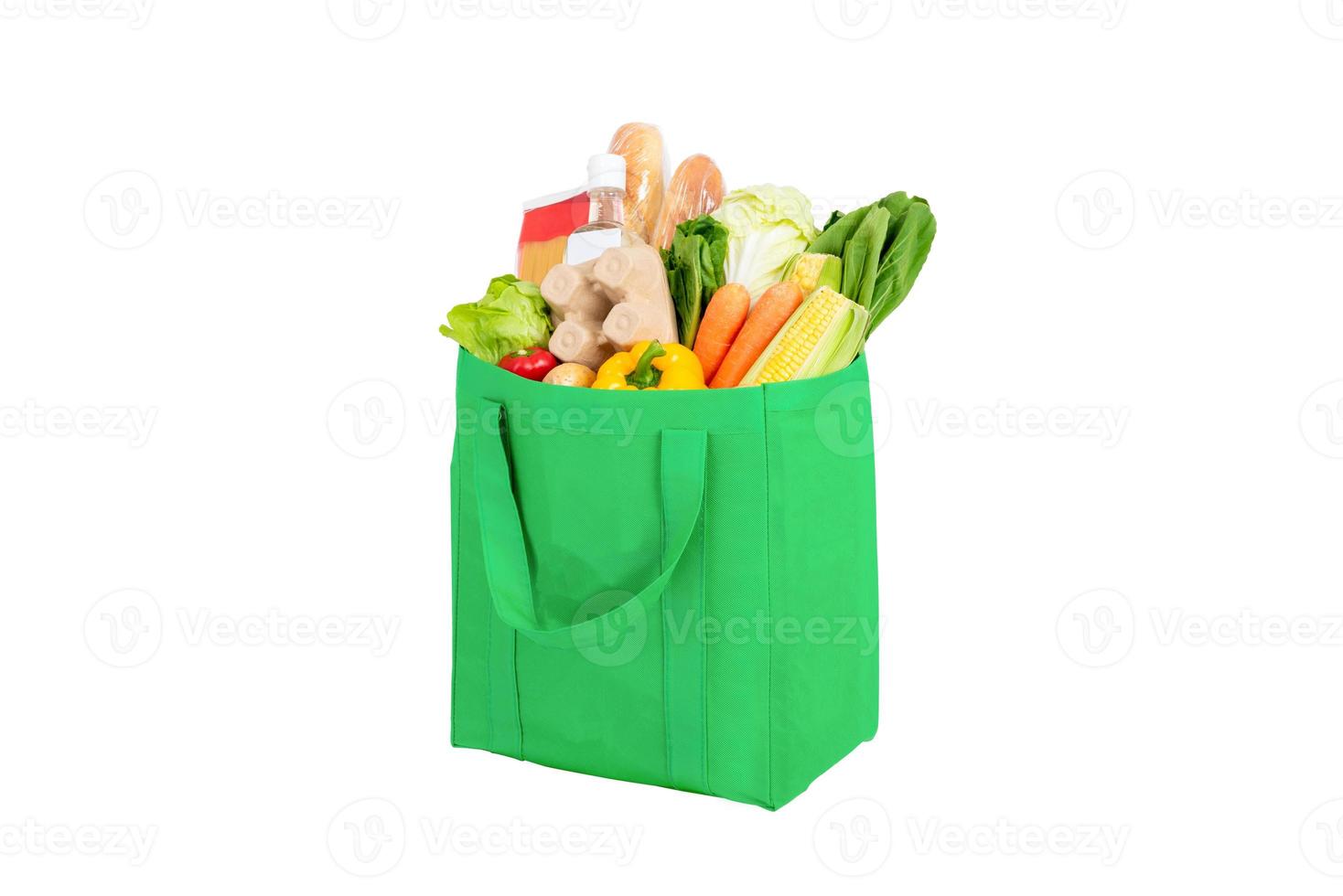 Bolsa de compras verde reutilizable llena de verduras y comestibles aislado sobre fondo blanco. foto
