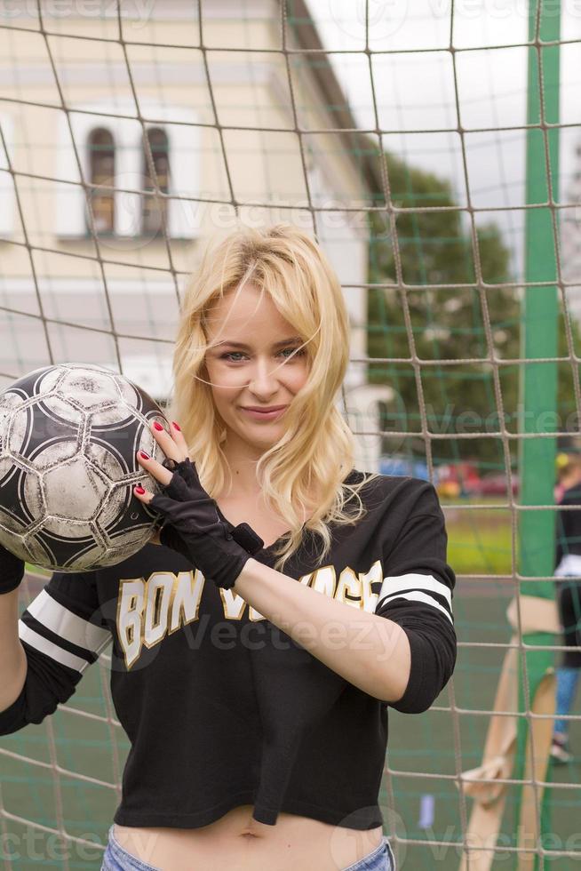 hermosa rubia con una pelota en la portería de fútbol. foto