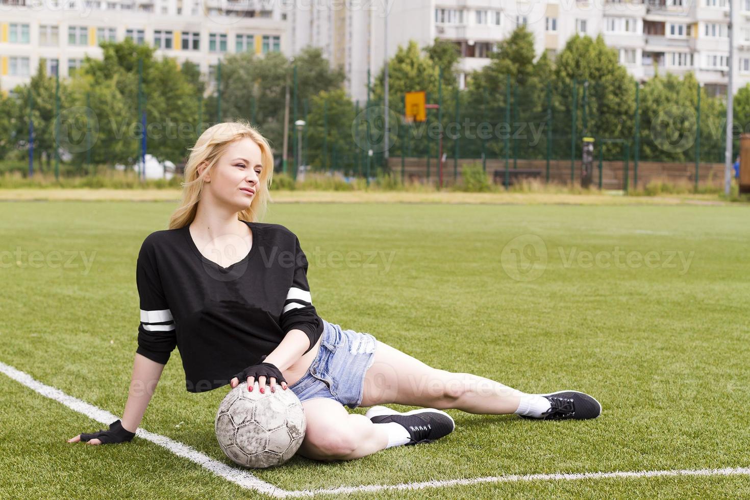 la niña está sentada en el campo de fútbol con la pelota. foto