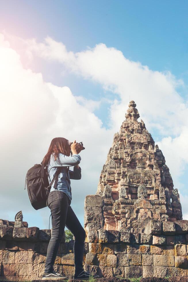 Young attractive woman photographer tourist with backpack coming to shoot photo at ancient phanom rung temple in thailand.