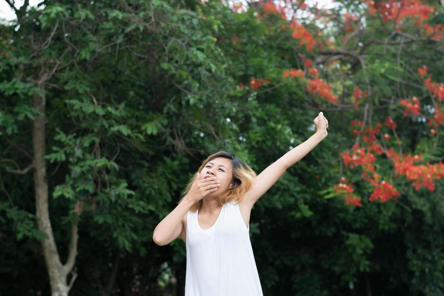 concepto de estilo de vida de las mujeres hermosa joven asiática estirándose y bostezando con aire fresco en el parque verde. foto