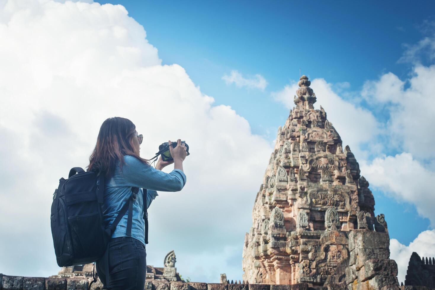 Young attractive woman photographer tourist with backpack coming to shoot photo at ancient phanom rung temple in thailand.