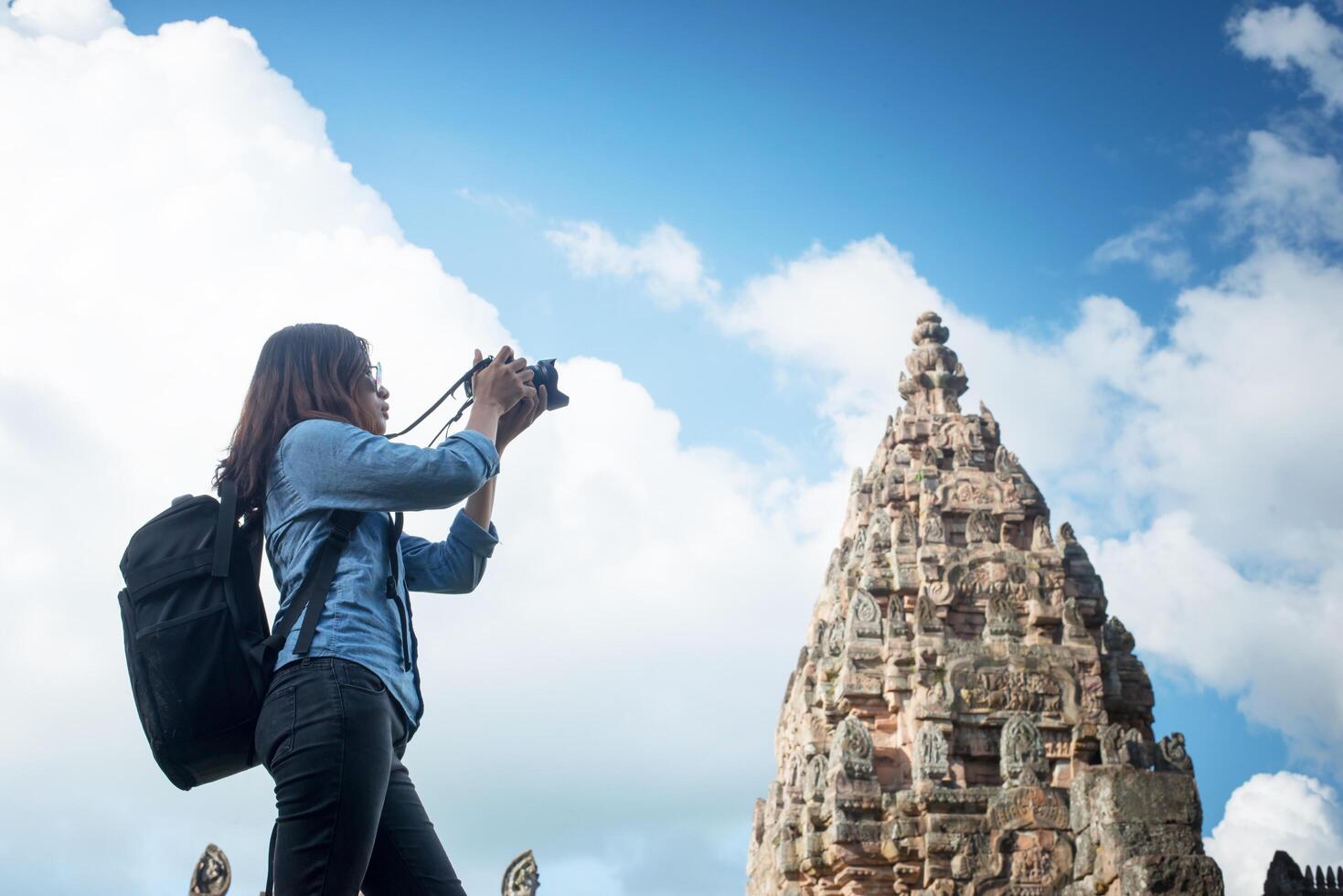 Young attractive woman photographer tourist with backpack coming to shoot photo at ancient phanom rung temple in thailand.