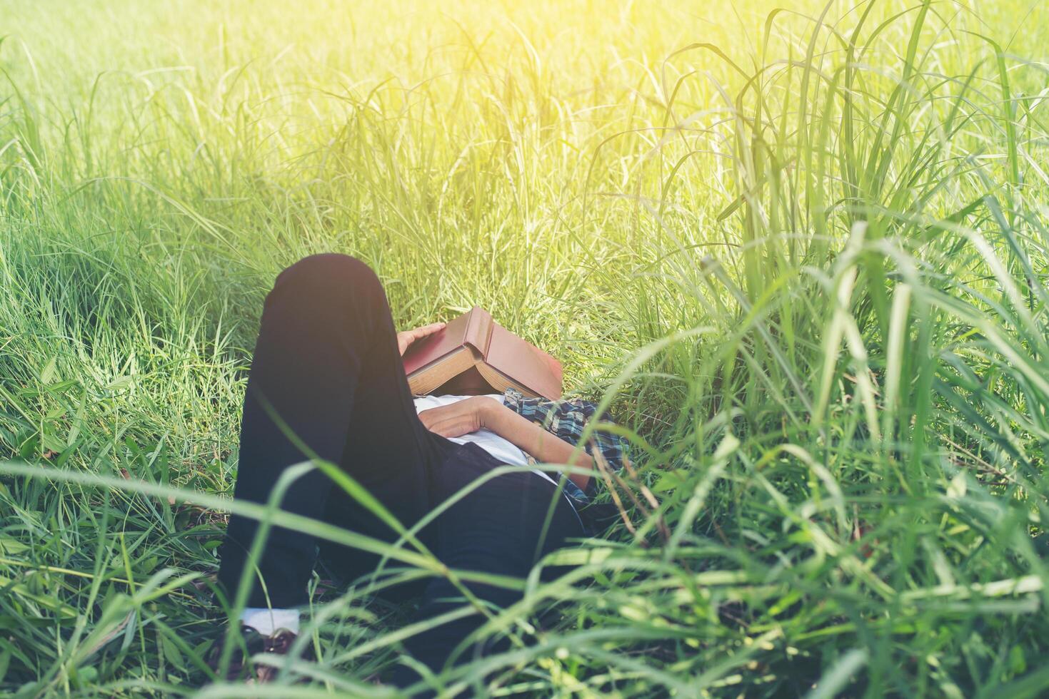 Young hipster man lying down on grassland napping tired after reading book with nature around. photo
