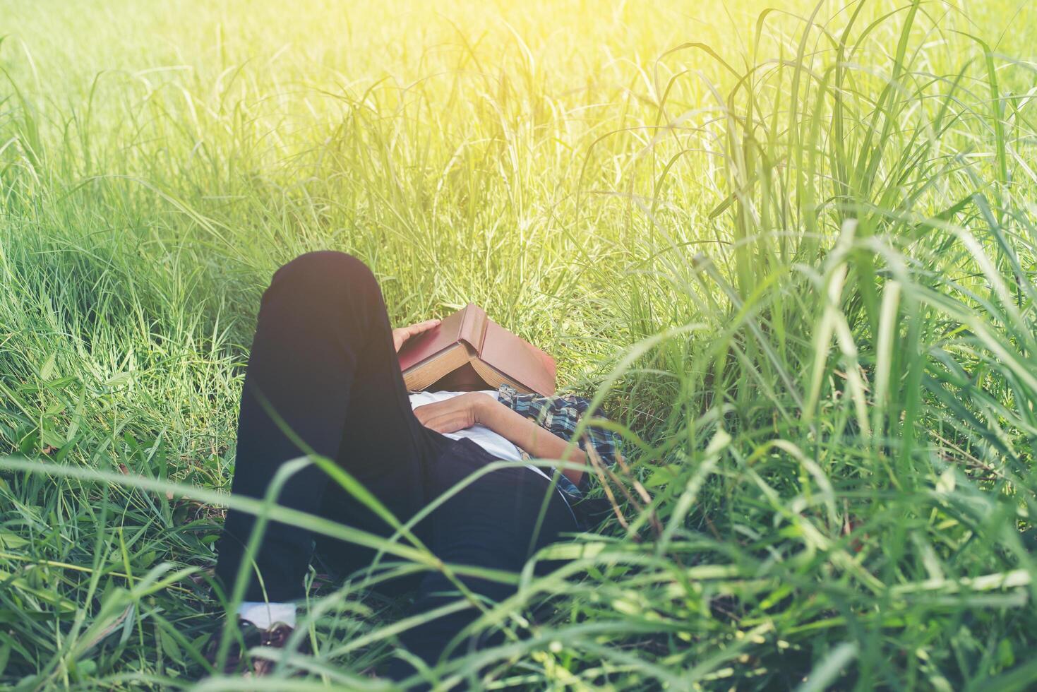 joven hipster acostado en los pastizales tomando una siesta cansado después de leer un libro con la naturaleza alrededor. foto