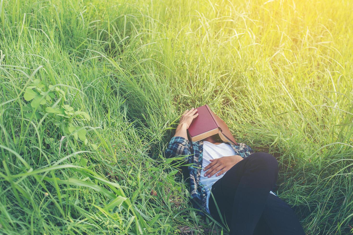 joven hipster acostado en los pastizales tomando una siesta cansado después de leer un libro con la naturaleza alrededor. foto