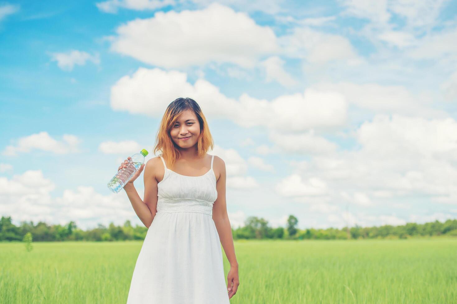 Women lifestyle concept young pretty  woman wearing white dress holding bottle of water at grassland smiley to camera look so fresh enjoy and happy. photo