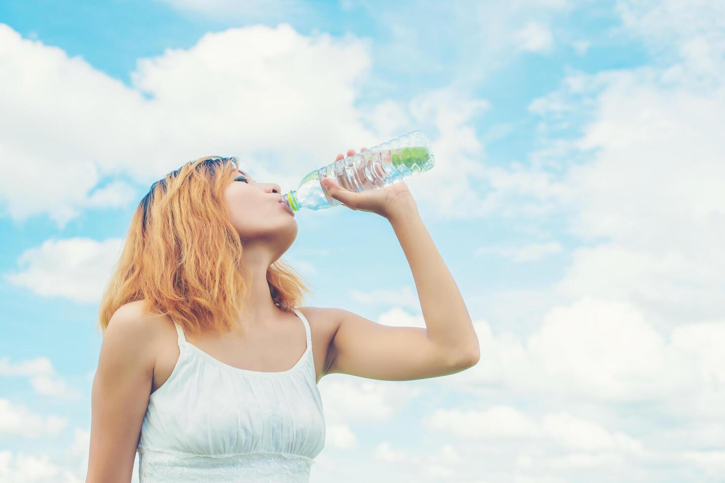 concepto de estilo de vida de las mujeres mujer hermosa joven con vestido blanco bebiendo agua en el parque verde de verano. foto