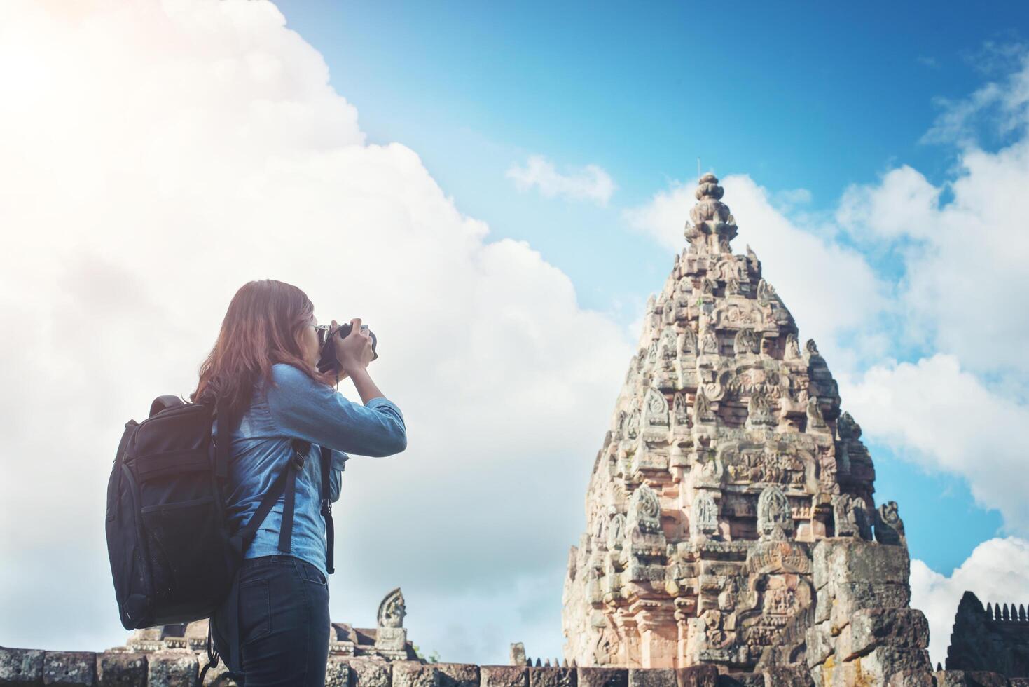 Young attractive woman photographer tourist with backpack coming to shoot photo at ancient phanom rung temple in thailand.