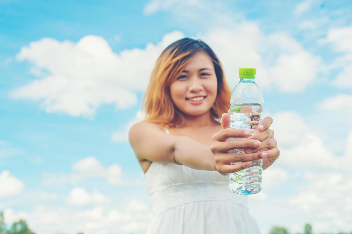 Women lifestyle concept young pretty  woman wearing white dress holding bottle of water at grassland smiley to camera look so fresh enjoy and happy. photo