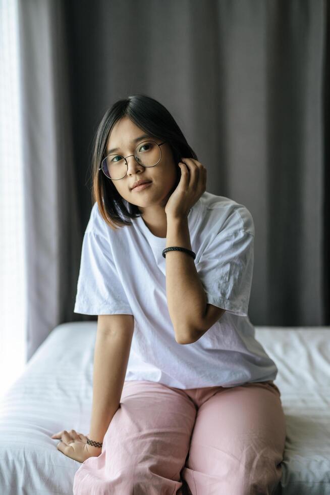 una mujer con una camisa blanca sentada en la cama y mirando hacia afuera. foto