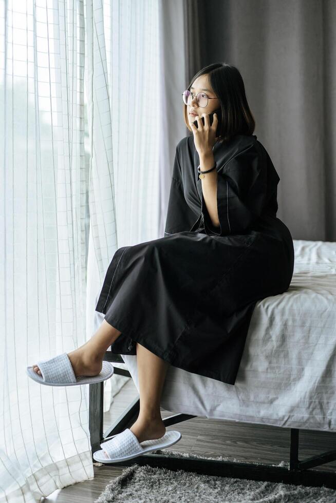 Woman wearing a white shirt, sitting on the bed and talking on the phone. photo