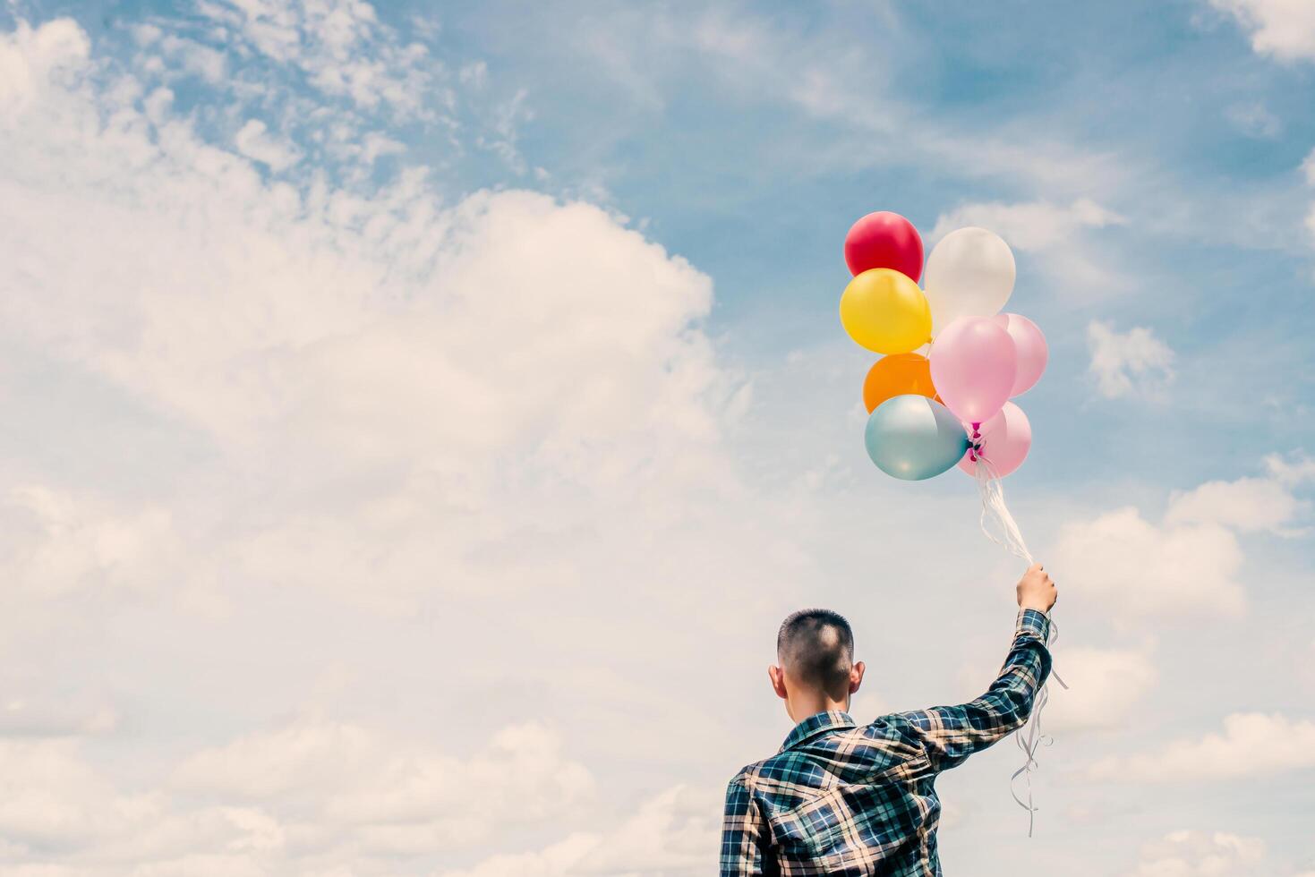 back of Happy young hipster man holding colorful balloons in grassland enjoy life and happy. photo