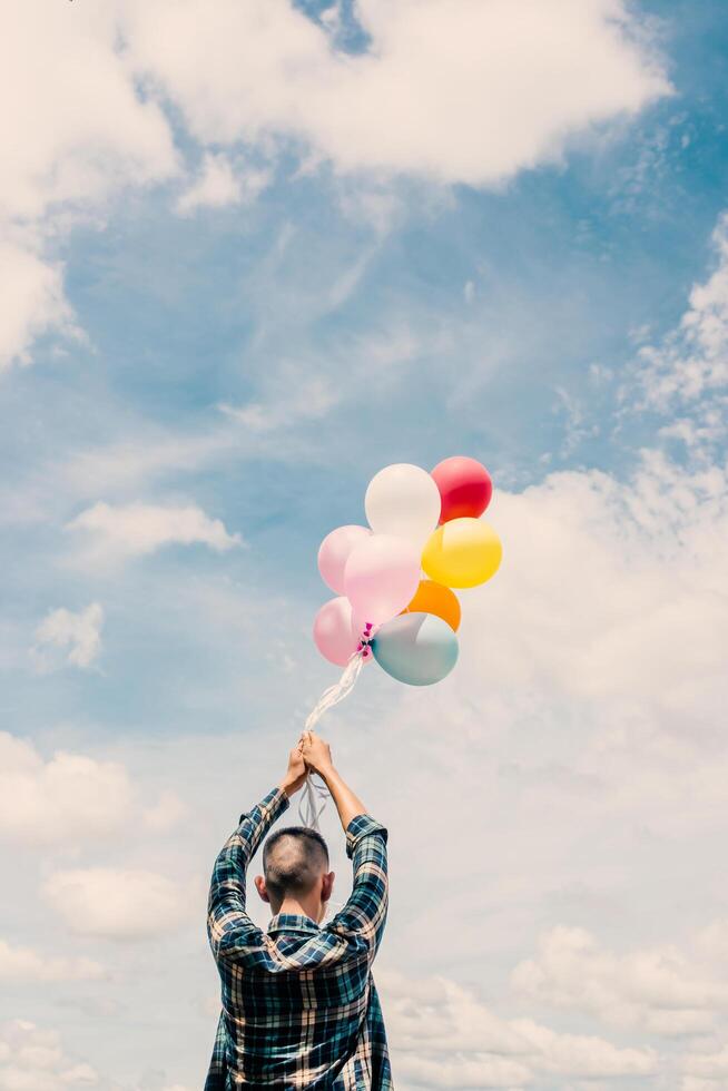 Happy young hipster man holding colorful balloons in grassland enjoy life and happy. photo