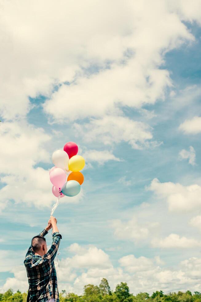 back of Happy young hipster man holding colorful balloons in grassland enjoy life and happy. photo