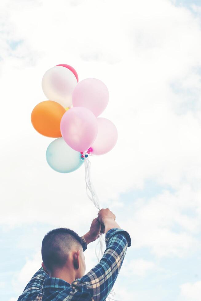 back of Happy young hipster man holding colorful balloons in grassland enjoy life and happy. photo