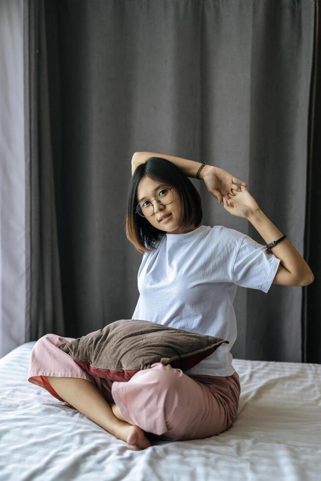 A woman in a white shirt sitting on the bed and raising both arms. photo