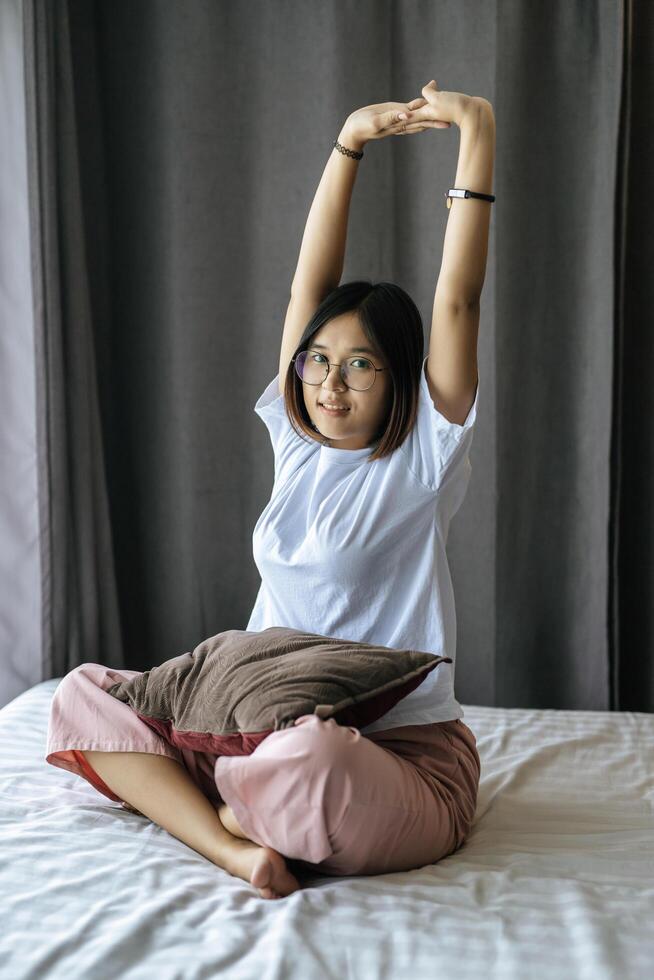 A woman in a white shirt sitting on the bed and raising both arms. photo