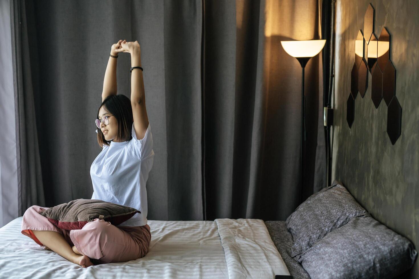 una mujer con una camisa blanca sentada en la cama y levantando ambos brazos. foto