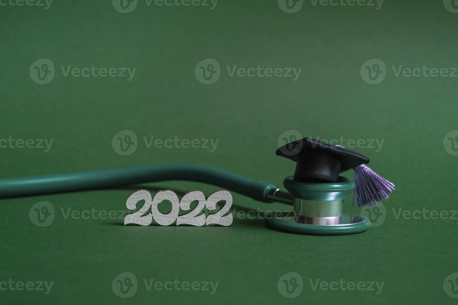 gorro de graduación con estetoscopio y números 2022 sobre fondo verde, primer plano con espacio de copia. concepto de educación médica. foto