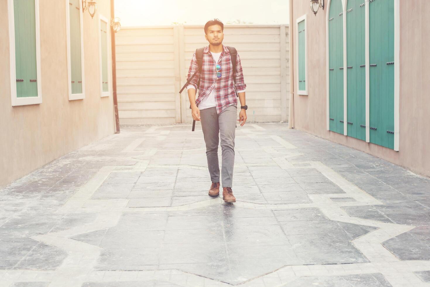 Young hipster man walking on urban street with backpack on his shoulder, to adventure. photo