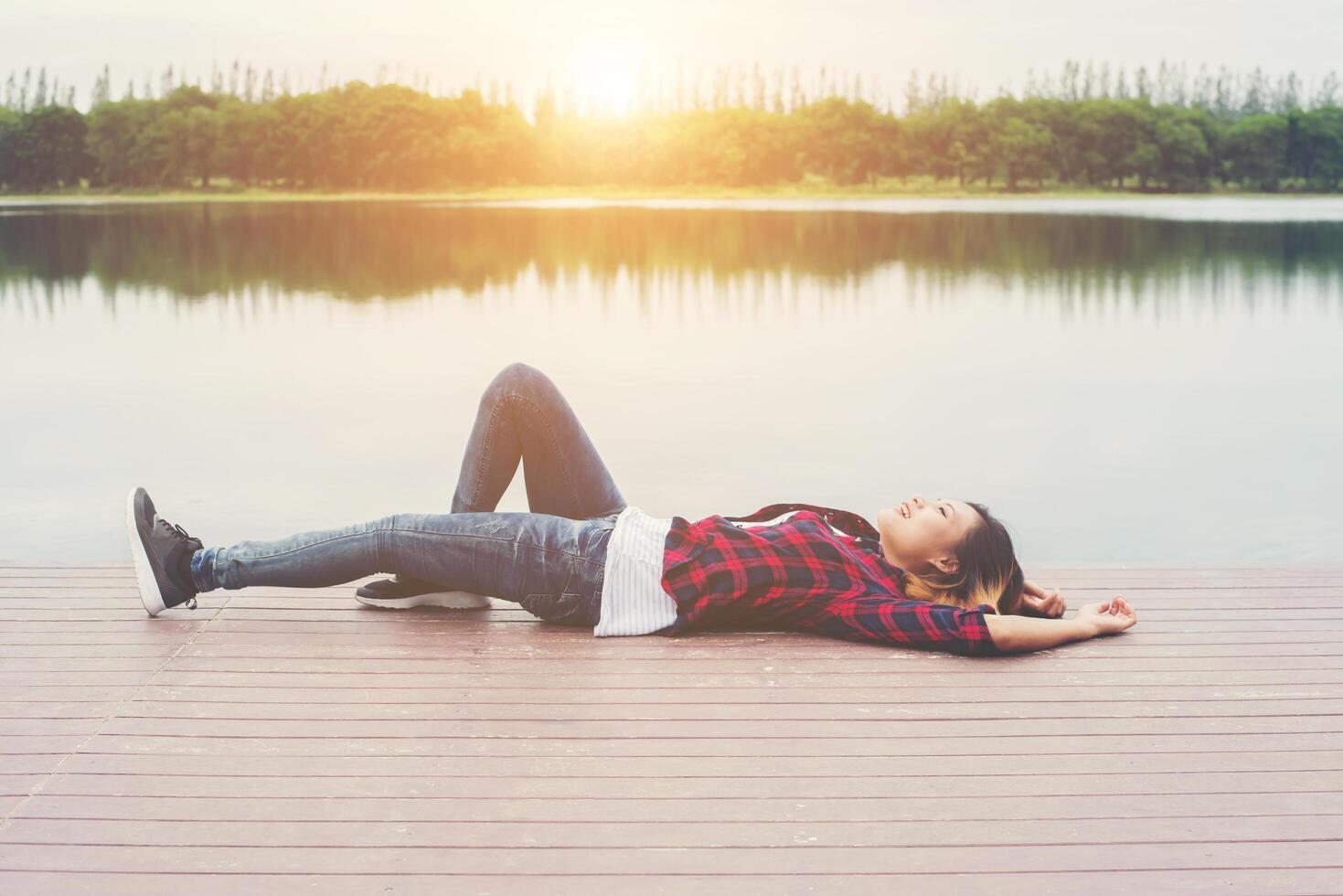 una joven hipster feliz se acostó en el lago del muelle, relajándose y disfrutando de la naturaleza. foto