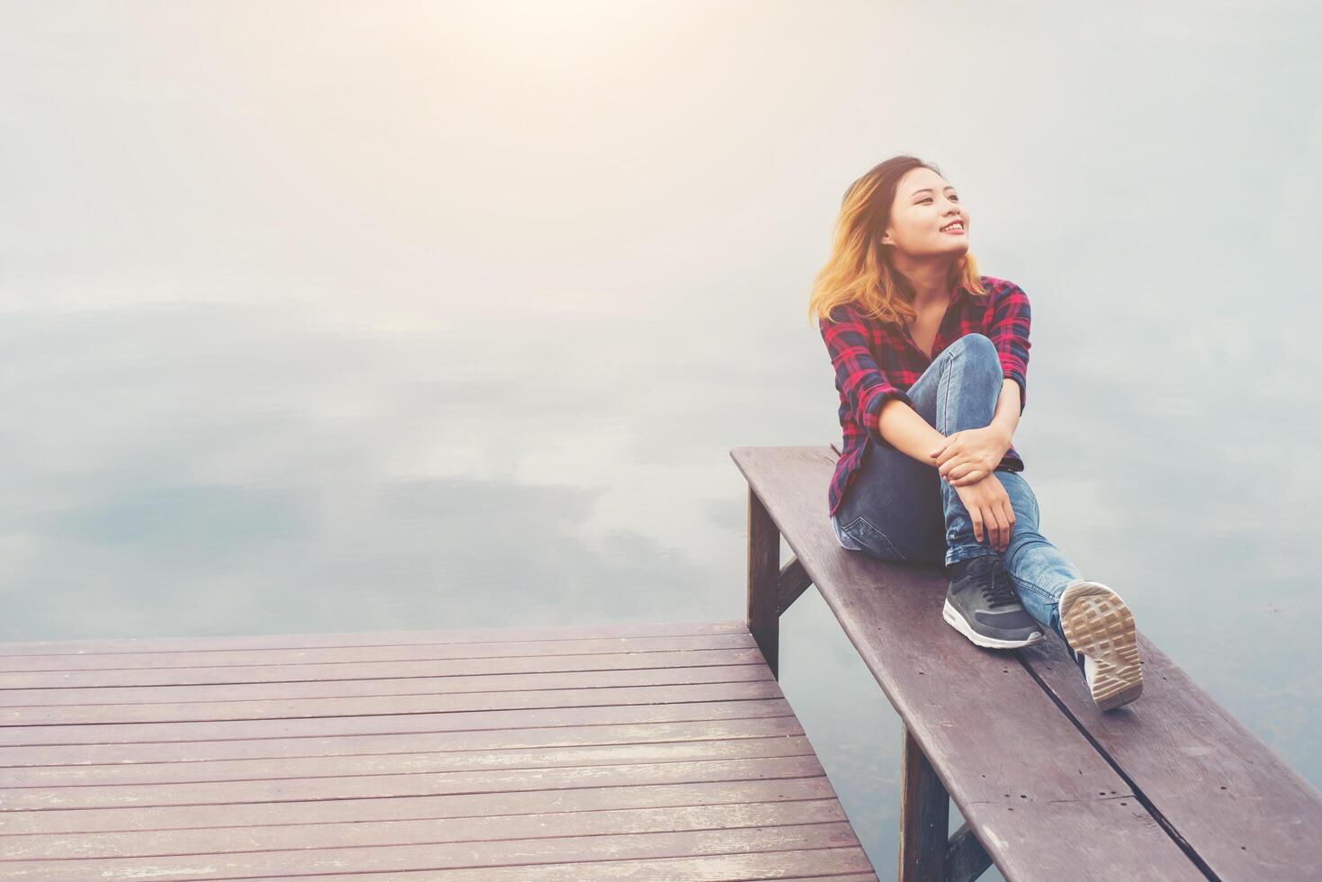 Happy young hipster woman sitting at the pier lake,relaxing enjoy with nature. photo