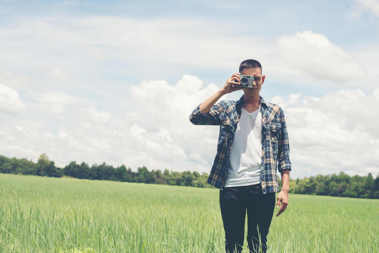 fotografía de hombre guapo joven hipster de pie disparando una cámara retro con la naturaleza disfruta y feliz en los pastizales. foto