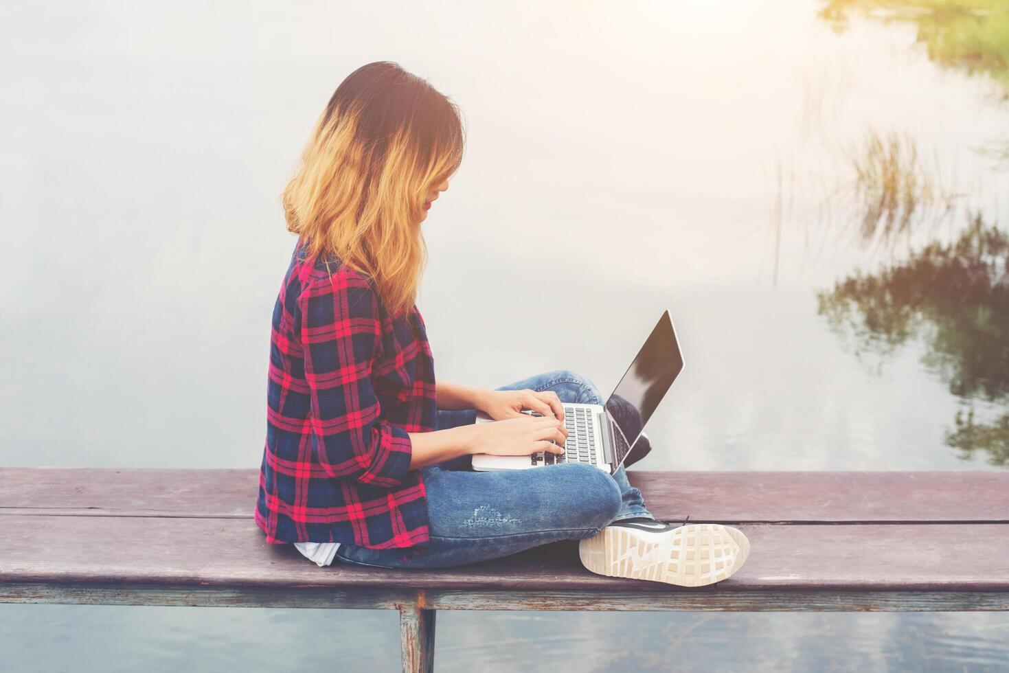 Young happy hipster woman working with her laptop sitting on pier,relaxing enjoy with nature. photo