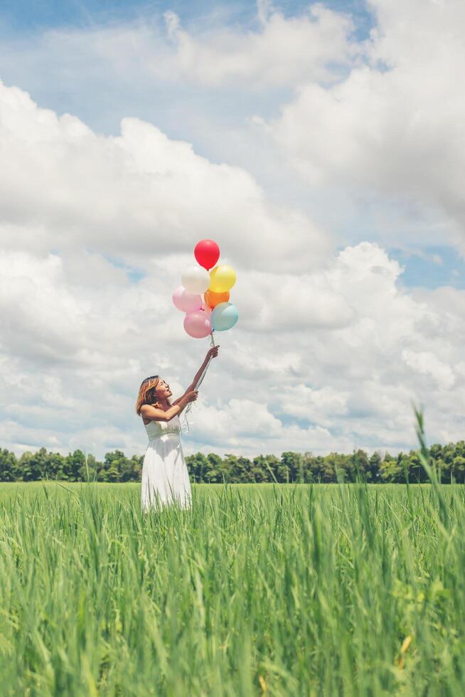 feliz joven hermosa mujer sosteniendo globos en el campo de hierba disfruta con aire fresco. foto