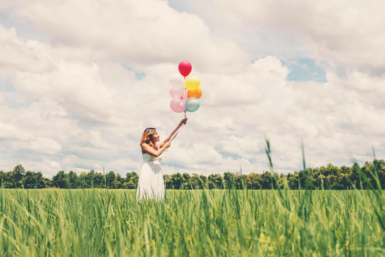 feliz joven hermosa mujer sosteniendo globos en el campo de hierba disfruta con aire fresco. foto