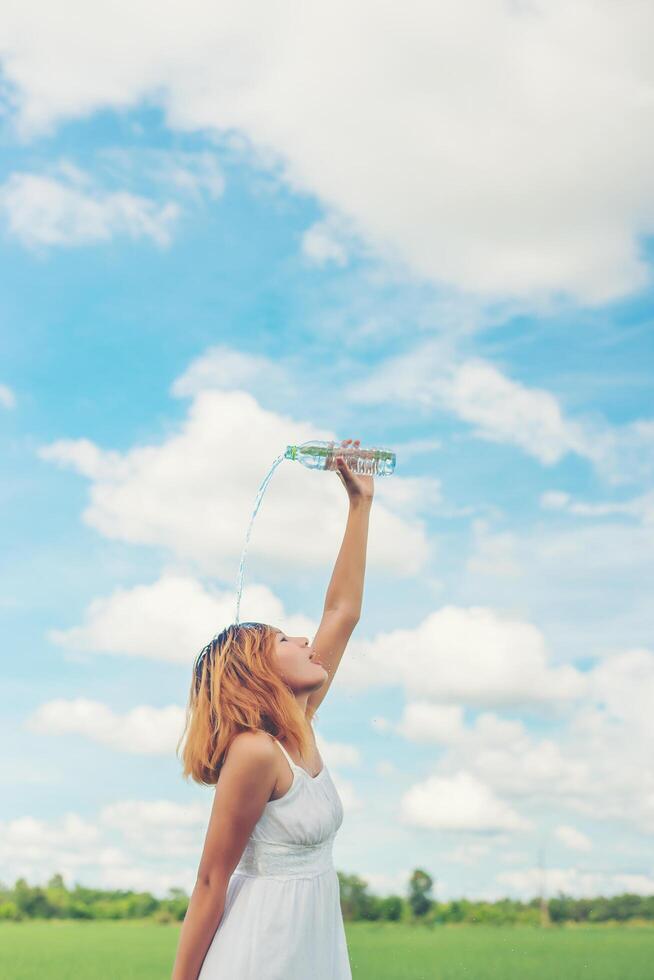 Young woman in park pours over a face for freshing at grassland enjoy and happy life. photo