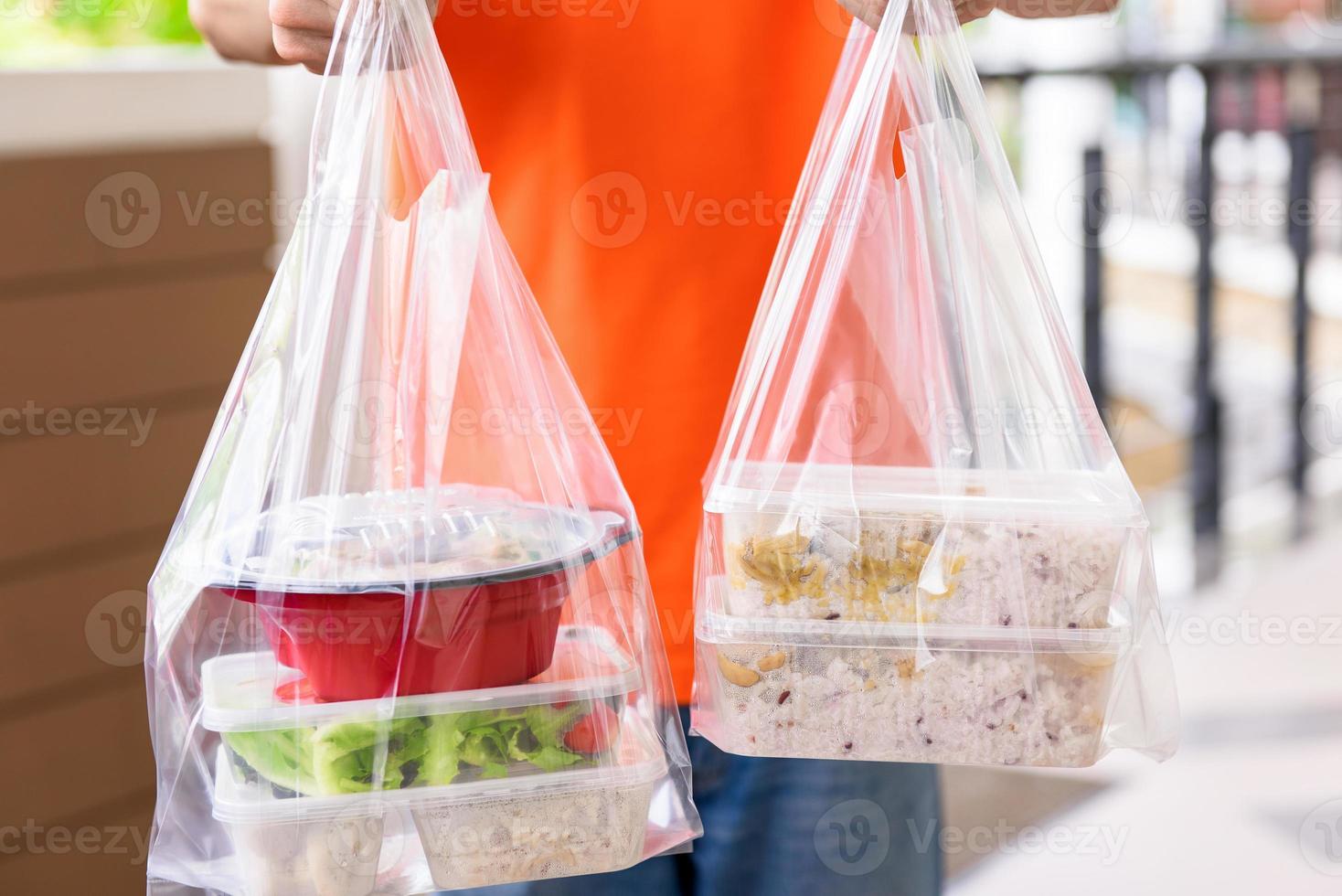 cajas de comida asiática en bolsas de plástico entregadas al cliente en casa por un repartidor con uniforme naranja foto