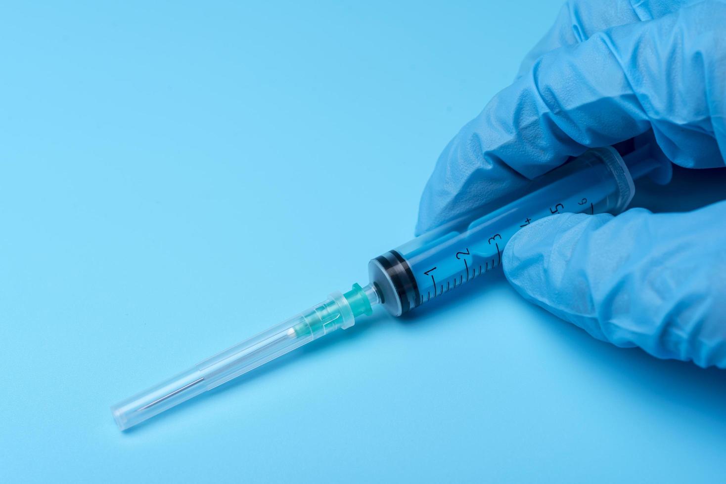 Hand in glove holding syringe on blue background. photo