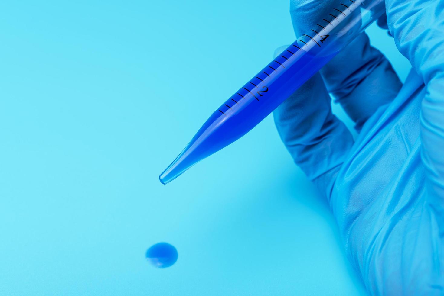 A gloved hand holding a laboratory pipette with blue liquid. photo