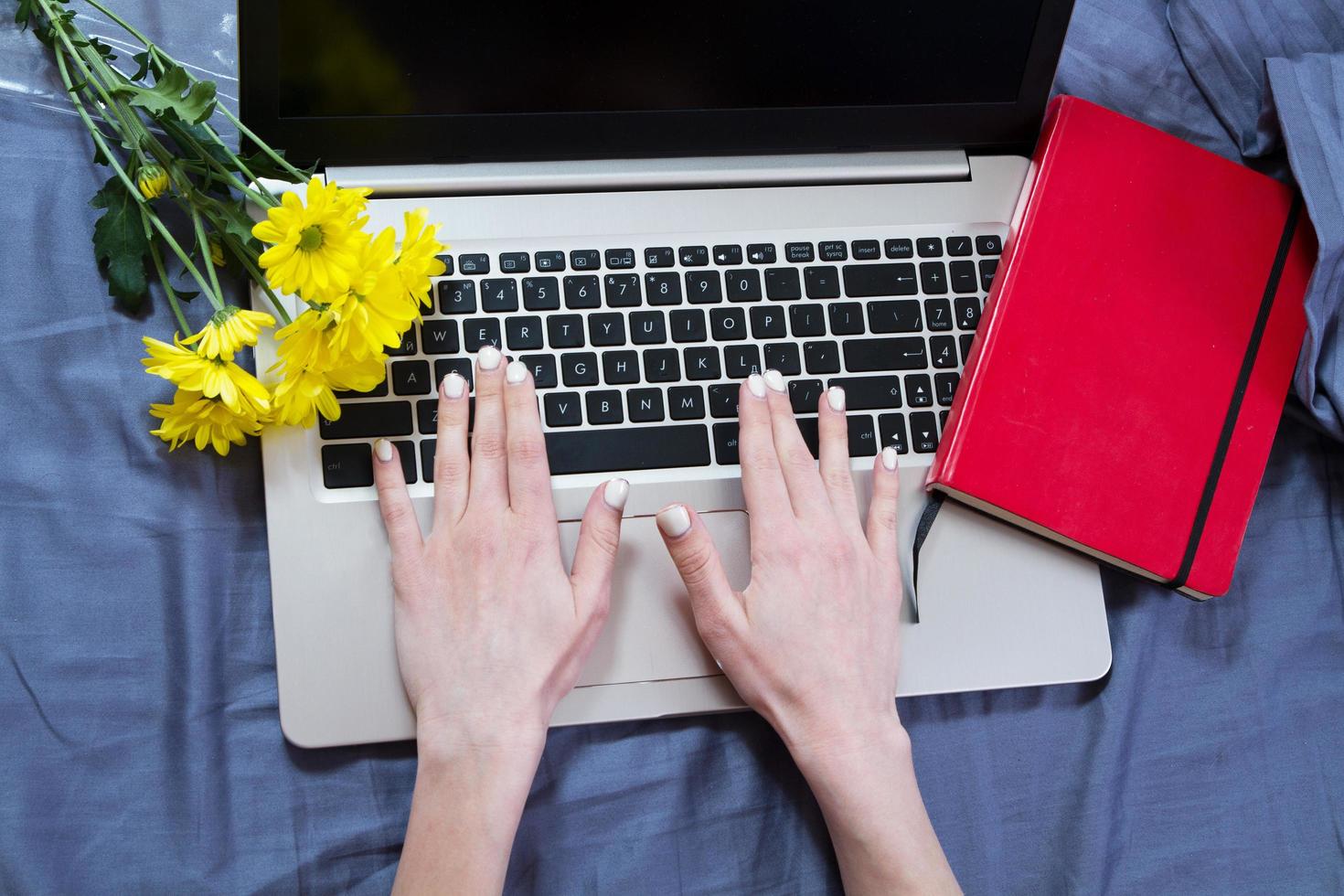 Work space at home, keyboard top view, female hand close up, notebook, work space on bed top view, flowers, colour background photo