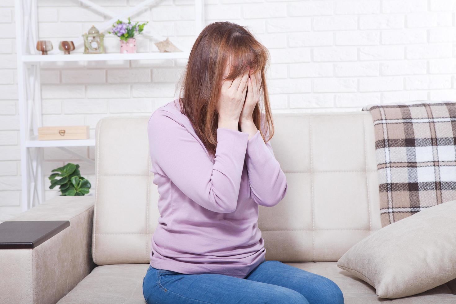 Beautiful middle aged brunette woman crying on sofa. Home background. Menopause time. Copy space and mock up photo