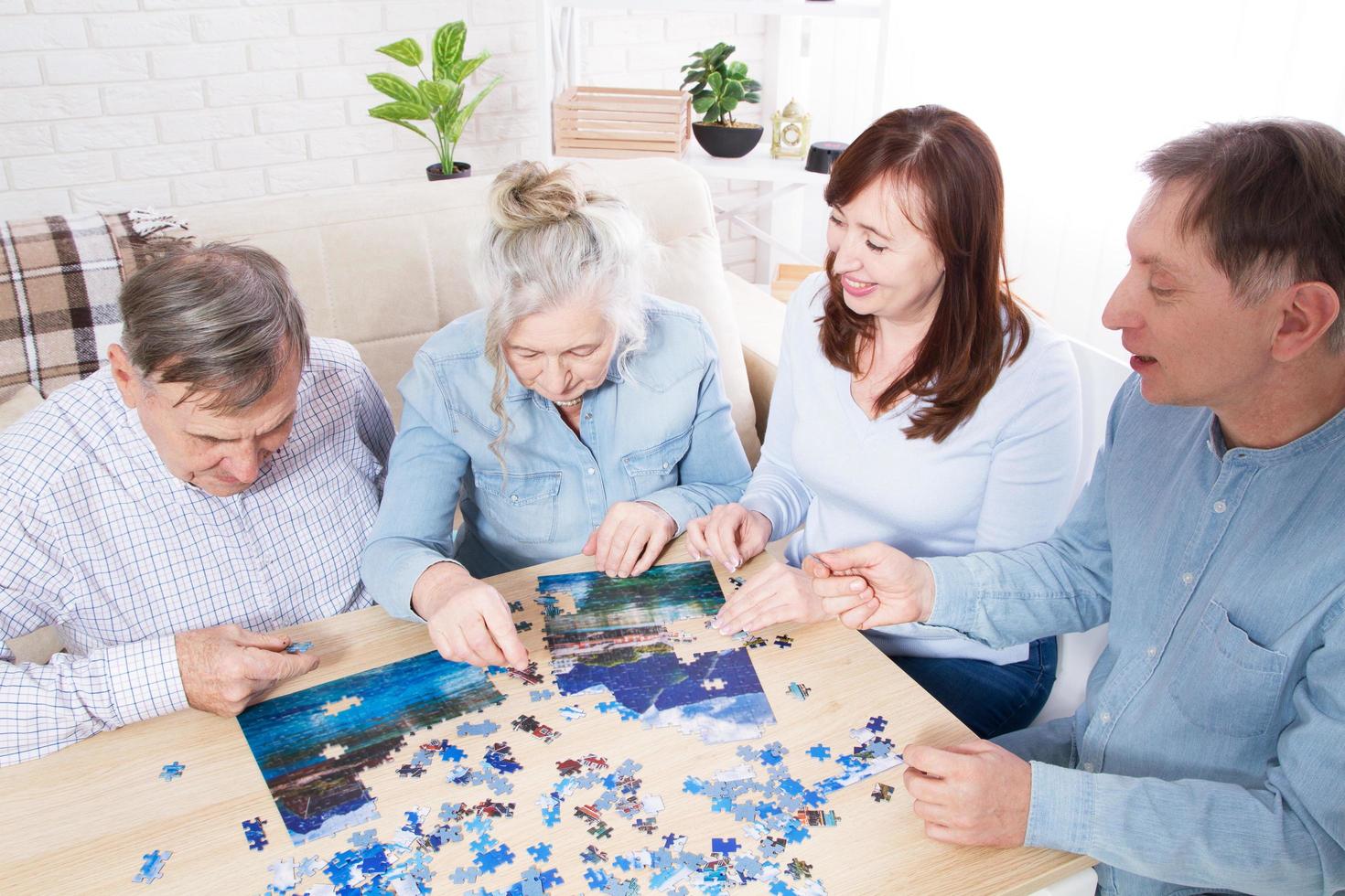 juego familiar en rompecabezas en casa, pareja de ancianos y pareja de mediana edad trabajando juntos en un rompecabezas en casa foto