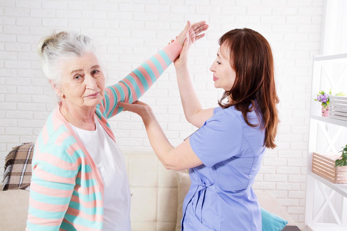 Physiotherapist is conducting a rehabilitation lesson with an elderly woman at home or in a clinic. photo