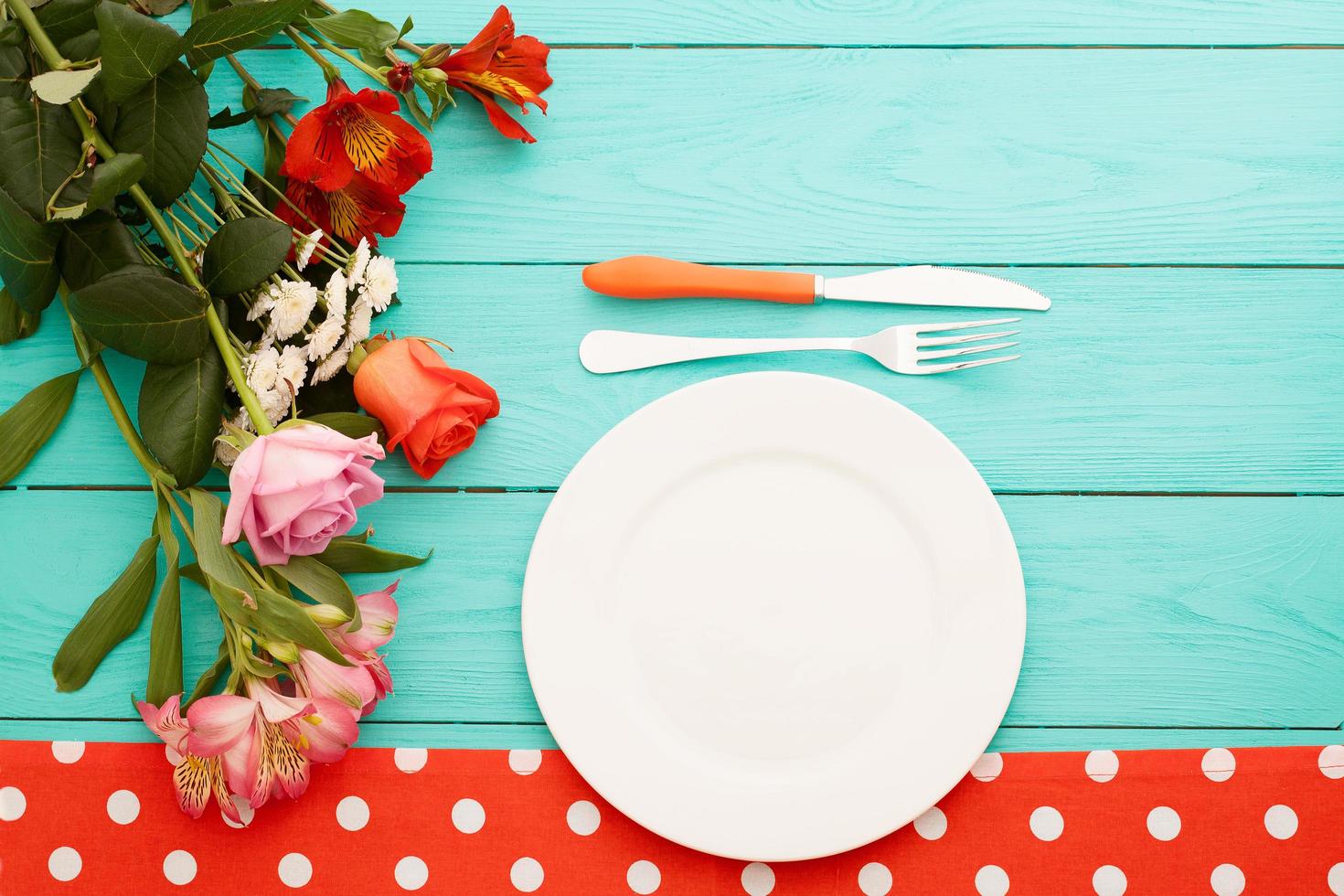 cena festiva con cubiertos, cuchillo, tenedor, plato y rosas sobre fondo de madera azul. vista superior. Bosquejo. flores copie el espacio foto