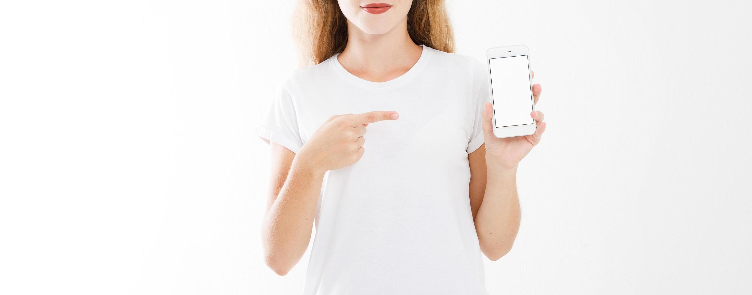 young girl, woman in t-shirt pointing finger at blank screen mobile phone isolated on white background. Hand holding smartphone. Copy space photo