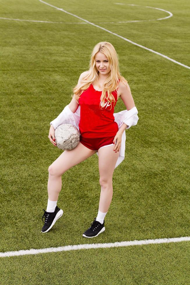 rubia con una pelota en el campo de fútbol con uniforme rojo. foto