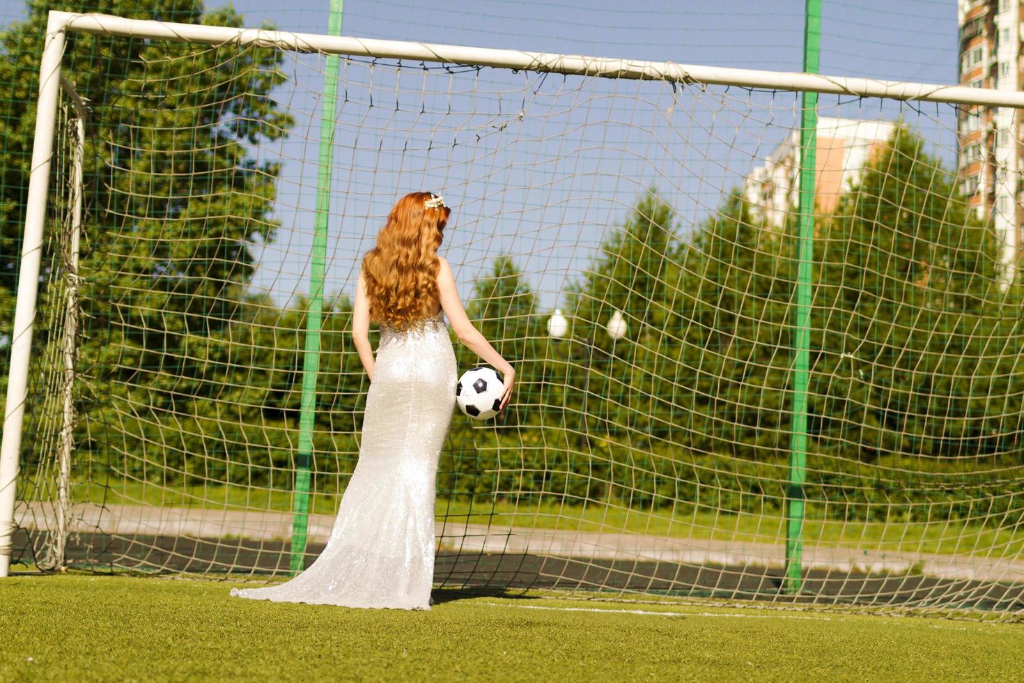 A girl with red hair stands at the football goal with her back and the ball. photo