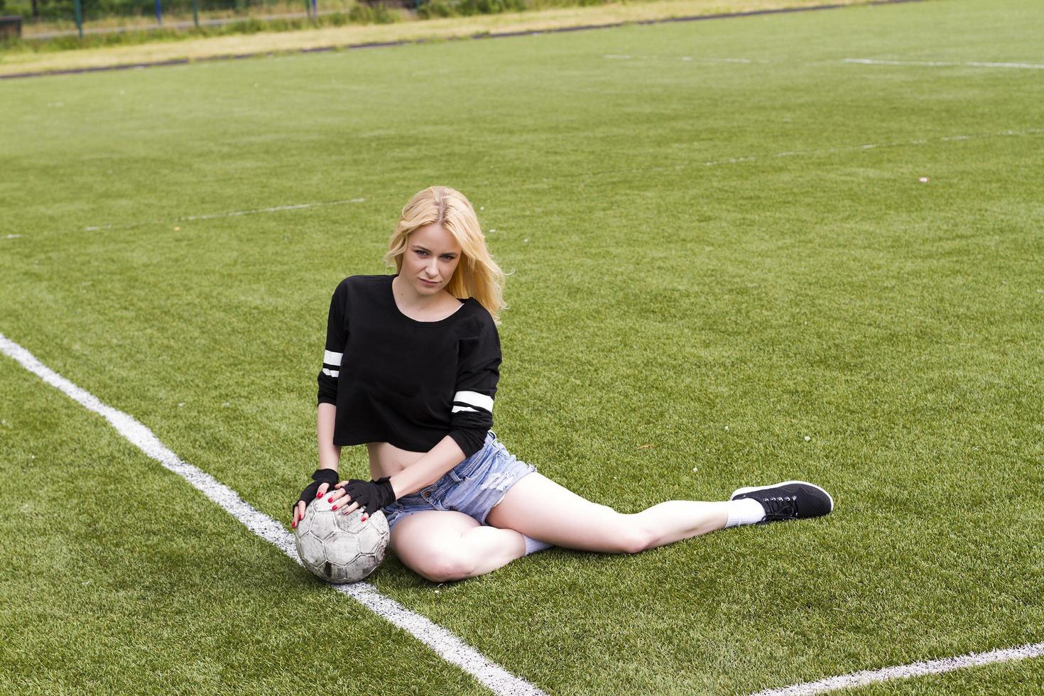 The girl is sitting on the football field with the ball. photo