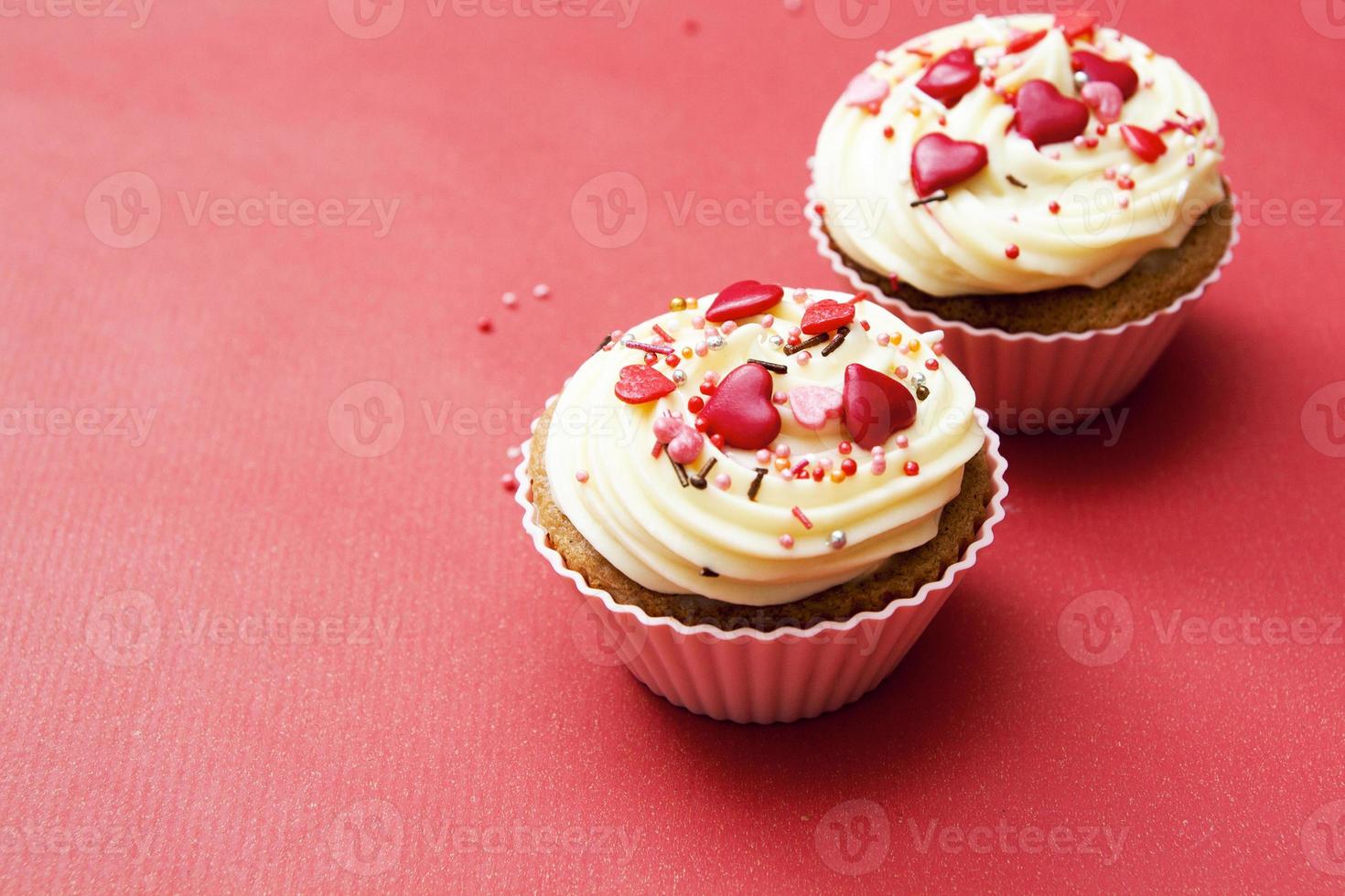 Close-up of two cupcakes with cream and heart decor on red background. Composition for Valentines Day with copy space photo